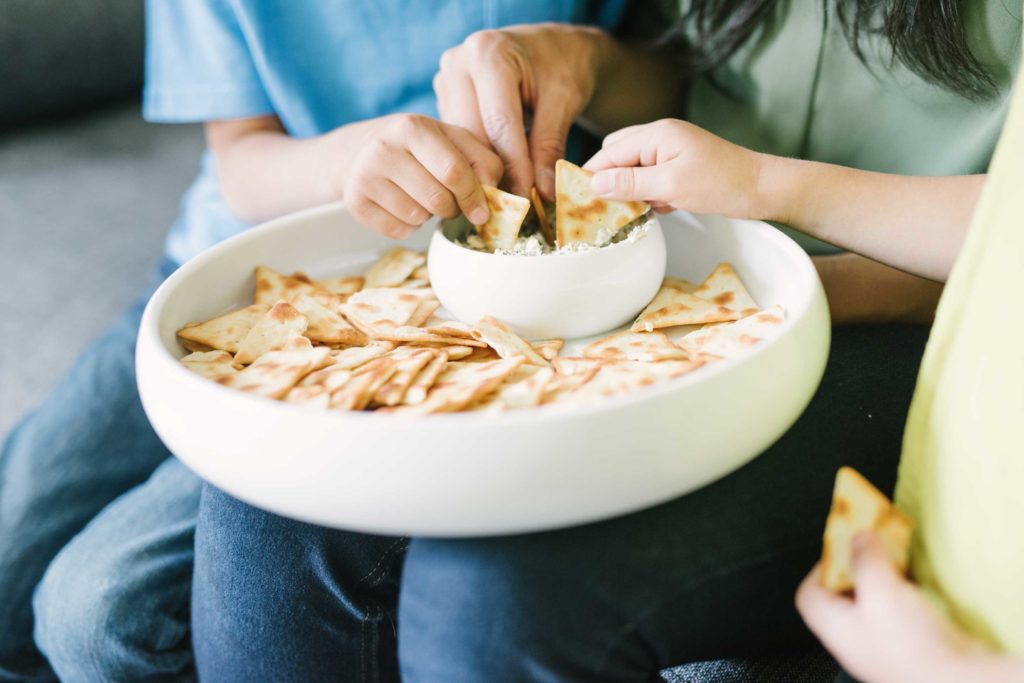 hands dipping pita chips in a bowl of La Terra Fina Dip