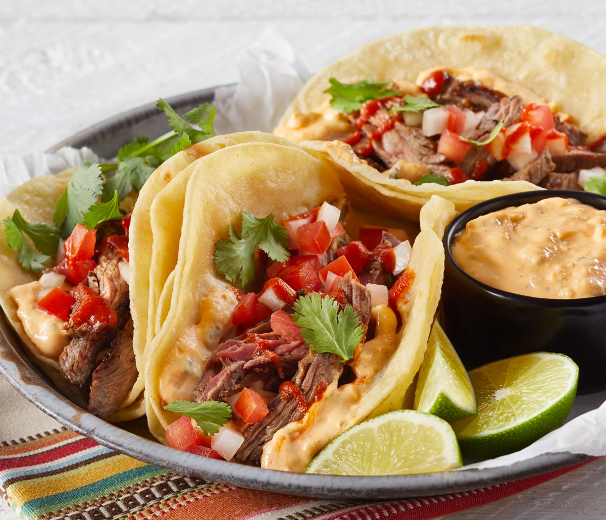 Steak Sriracha Soft Tacos on a plate with dip and limes