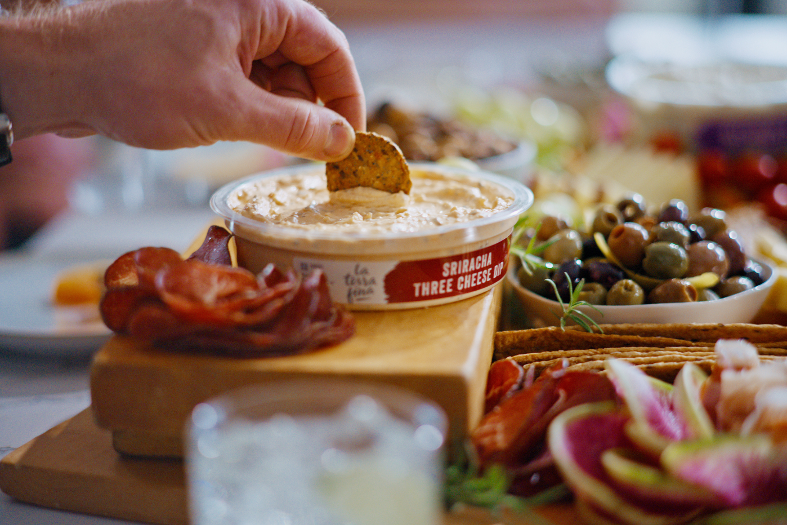 Hand dipping a cracker into La Terra Fina Sriracha Three Cheese Dip